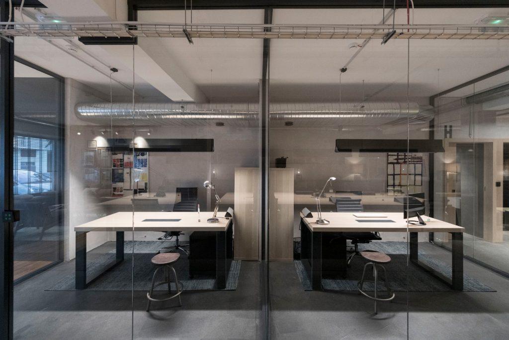Gabinete de equipa privado no Outglocal Coworking Aveiro, visto através da divisória de vidro, com amplas secretárias de trabalho.