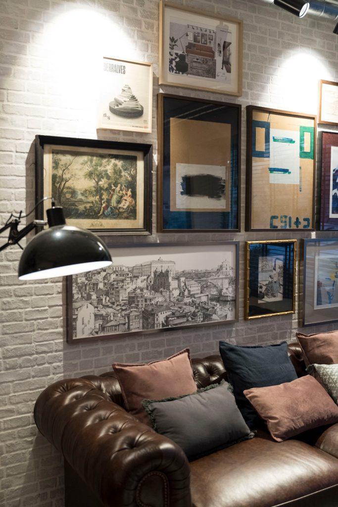 Pormenor da área de lounge no Outglocal Coworking Aveiro, com um sofá de cabedal e uma parede de galeria com vários quadros.