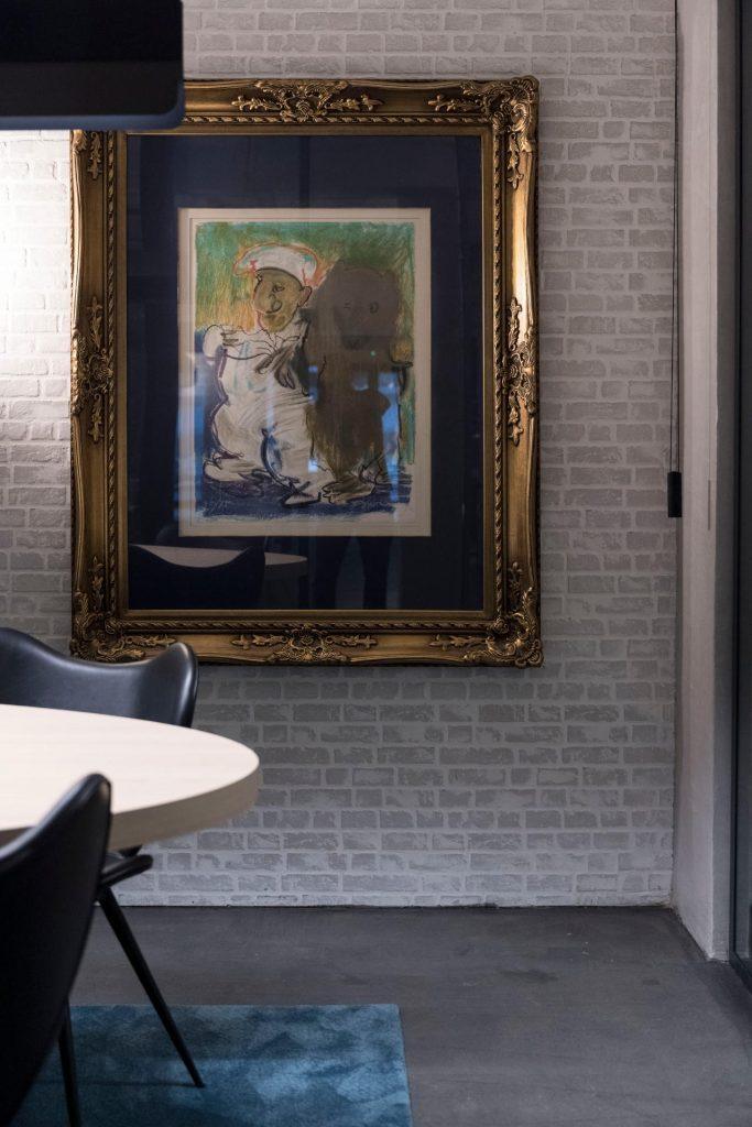 Pormenor de um quadro de arte com moldura dourada na parede de tijolo branco da sala de reuniões da Outglocal Aveiro.