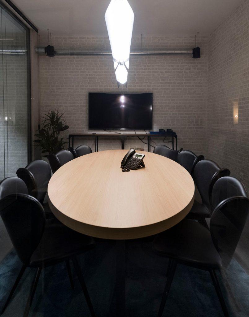 Sala de reuniões no Outglocal Coworking Aveiro com mesa redonda em madeira, cadeiras pretas e ecrã de apresentação ao fundo.